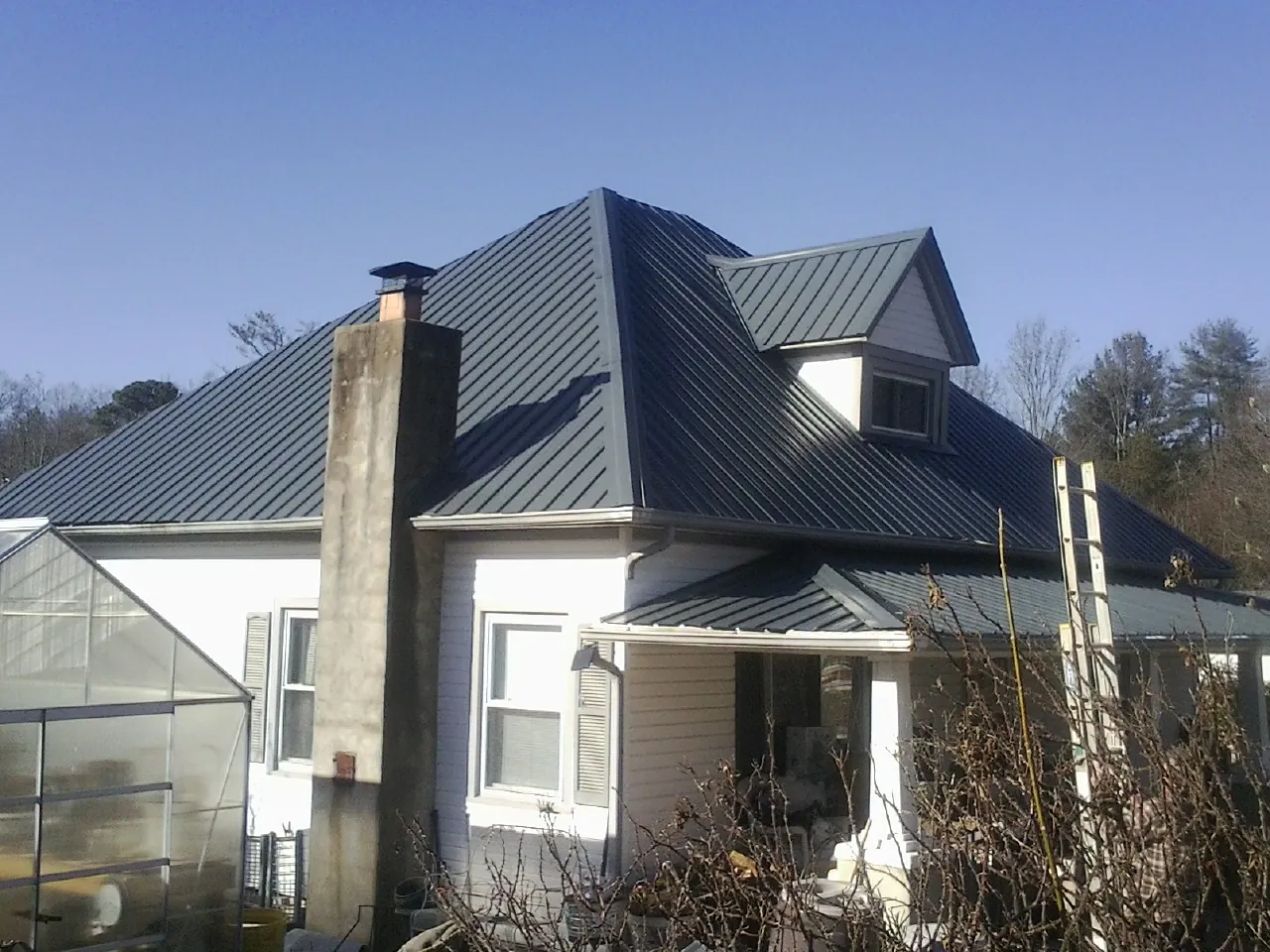 Dark blue standing seam metal roof on a white farmhouse with dormer in West Sand Lake
