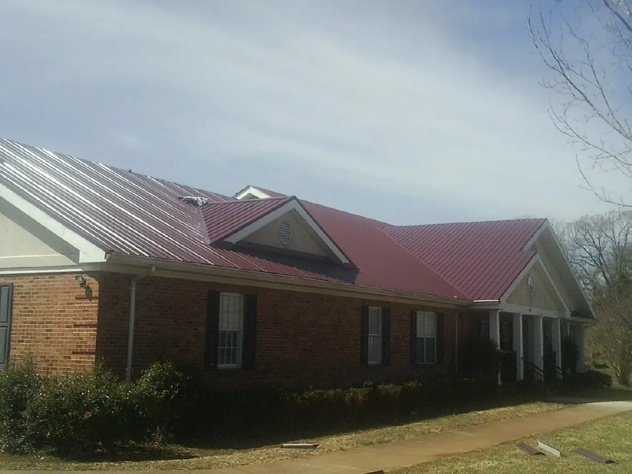 Red metal roof with gabled entries on a long brick building, from a Hail Damage Roof Repair job in West Sand Lake