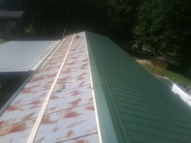 Old rusted panels beside newly installed green metal roofing — Wind Damage Roof Repair by Roofing Brothers in West Sand Lake