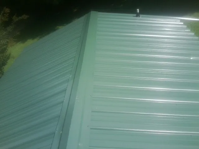New green metal panels meeting at the ridge of a roof — Flat Roof Repair work by our crew in West Sand Lake