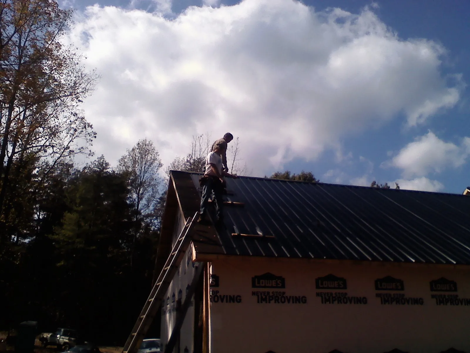 Roofer fastening dark metal panels high against a cloudy sky, from a Roof Inspection job in West Sand Lake