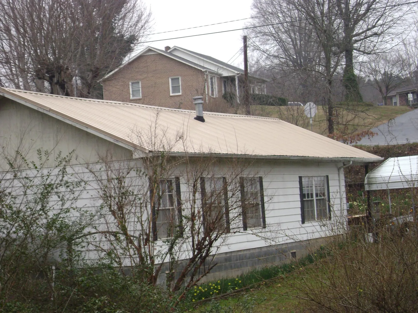 Tan metal roof on a white sided house set into a hillside — Commercial Roofing by Roofing Brothers in West Sand Lake