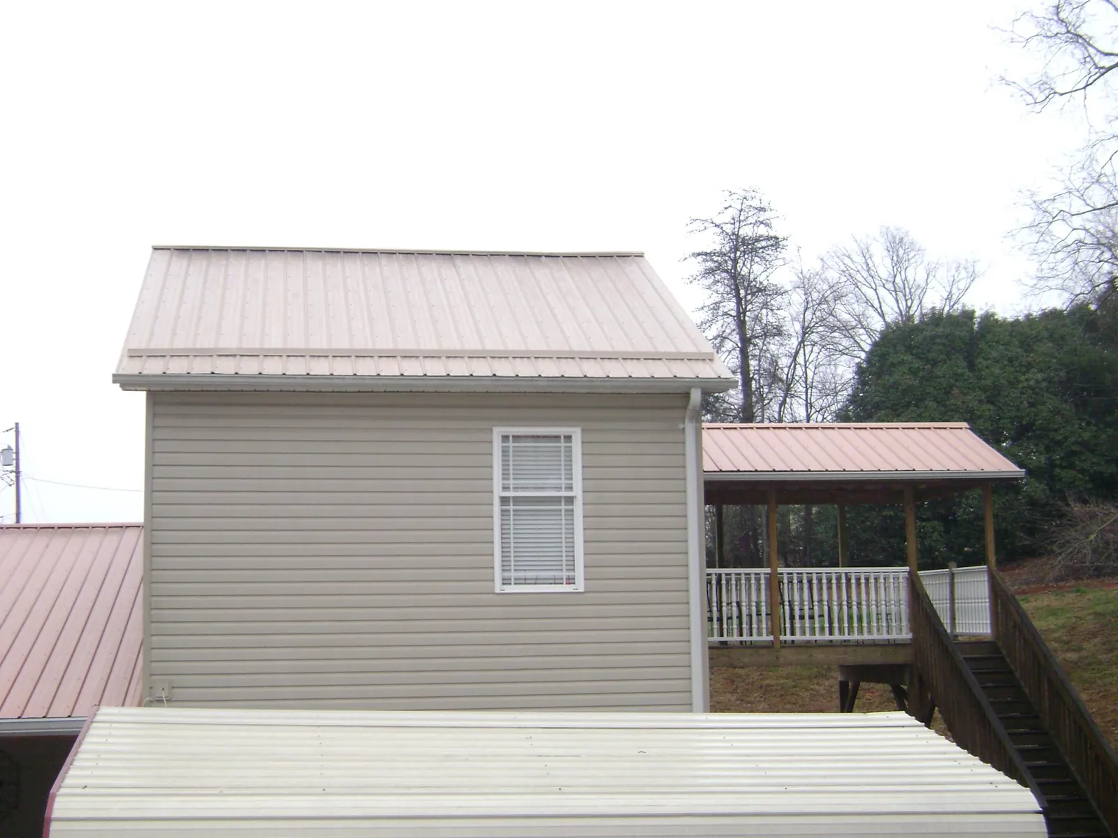 Tan metal roofs on a two story addition and attached porch, from a Roof Replacement job in West Sand Lake